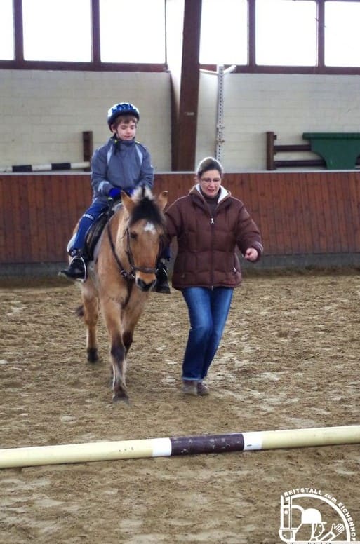 Eine Betreuerin führt ein Kind auf dem Pony durch die Halle