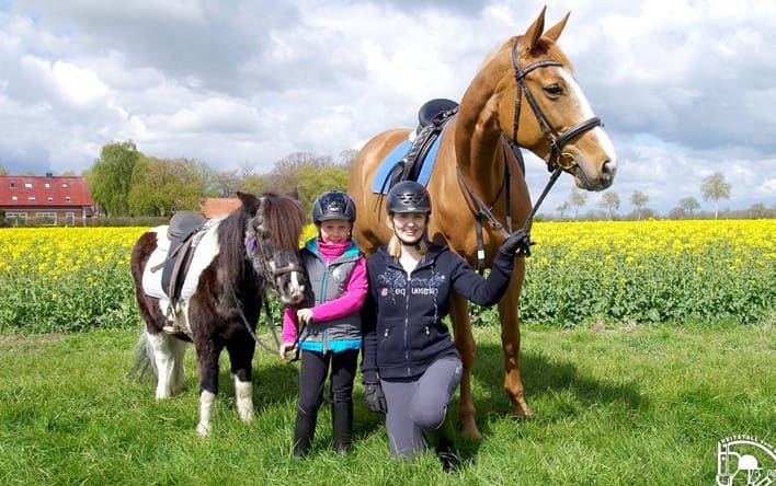 Reitkinder mit Pony und Pferd vor dem blühenden Rapsfeld